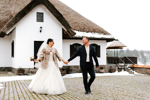 Hochzeitspaar vor ländlichem Gebäude mit Strohdach im Winter